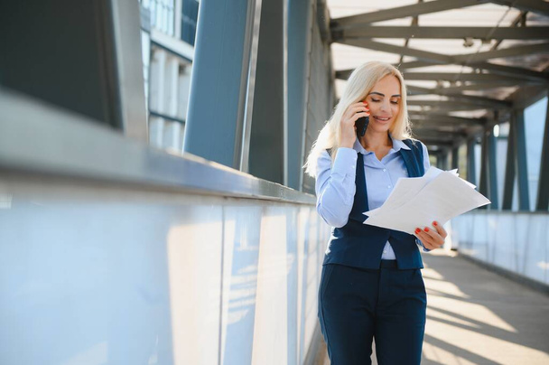 Business Woman With Phone Near Office. Portrait Of Beautiful Smiling Female In Fashion Office Clothes Talking On Phone While Standing Outdoors. Phone Communication. High Quality Image - Valokuva, kuva