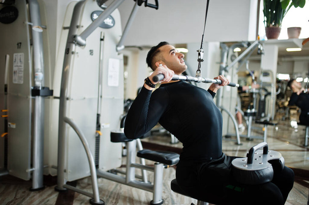 Muscular arab man training and doing workout on fitness machine in modern gym. - Φωτογραφία, εικόνα