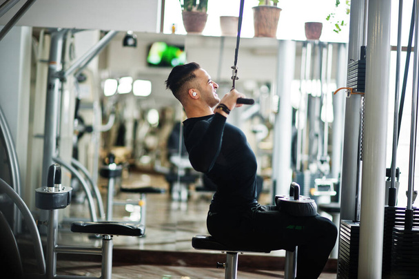 Muscular arab man training and doing workout on fitness machine in modern gym. - Foto, Imagem