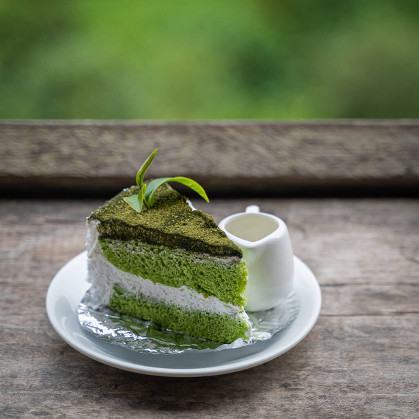 Green tea cake and leaf tea topping on a white plate at the wooden table. Favorite sweet and delicious dessert for relaxing to enjoy eating on a good day. - Φωτογραφία, εικόνα