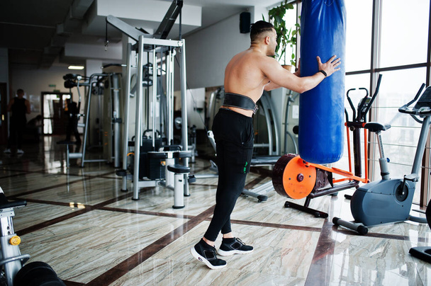 Muskelkräftiges arabisches Männertraining in modernen Fitnessstudios. Fitness arabische Männer mit nacktem Oberkörper machen Übungen mit Boxsack. - Foto, Bild