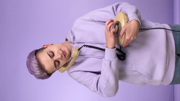 Vertikale Aufnahme einer jungen erwachsenen Person der Generation Z mit trendigem Look, die ein klassisches Schnurtelefon hält, mit Drehtelefon, Wählnummer, Gespräch, isoliert auf lila Hintergrund in Innenräumen - Filmmaterial, Video
