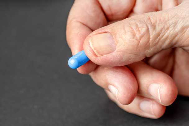 Old wrinkled hand holding a blue pill close up. Background with copy space. - Valokuva, kuva
