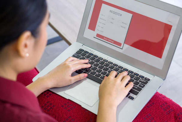 Молода азіатка в червоній сукні друкує на клавіатурі комп'ютера ноутбука, реєструючись для онлайн-застосунку знайомств на сайті
. - Фото, зображення