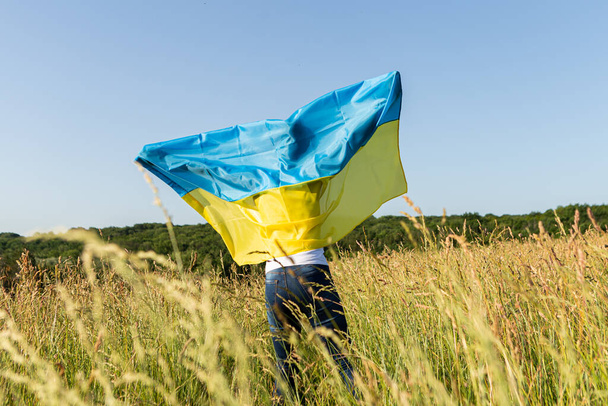 Αφροαμερικανή γυναίκα τυλιγμένη με ουκρανική κίτρινη μπλε σημαία κυματίζει στον άνεμο. Εθνικό σύμβολο της Ουκρανίας. Σταθείτε με την Ουκρανία, διεθνή υποστήριξη και αλληλεγγύη - Φωτογραφία, εικόνα