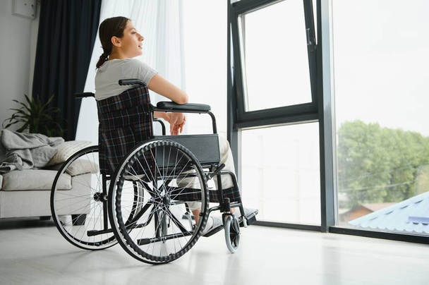 woman looking away while sitting in wheelchair at home. - Foto, immagini