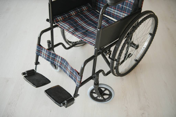 Empty wheelchair in living room next to the couch. - 写真・画像