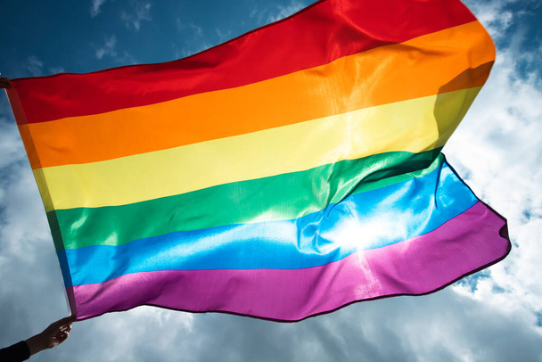 Bright rainbow LGBT flag fluttering against blue sky. LGBT community, happiness, freedom and love concept for same sex couples. - Foto, Imagen
