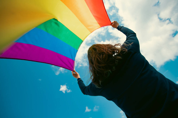Frau, die auf einer grünen Wiese mit einer schwulen Regenbogenfahne sitzt. bisexuell, schwul, lesbisch, transsexuell. Glück, Freiheit und Liebe für gleichgeschlechtliche Paare - Foto, Bild
