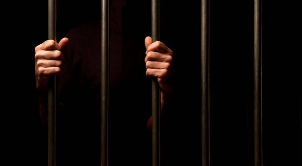 hands of a prisoner behind prison bars on black background - Foto, Imagem