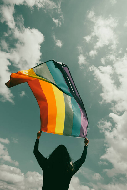 Woman sitting in a green meadow holding a Gay Rainbow Flag. Bisexual,gay, lesbian, transsexual symbol. Happiness, freedom and love concept for same sex couples - Foto, Bild
