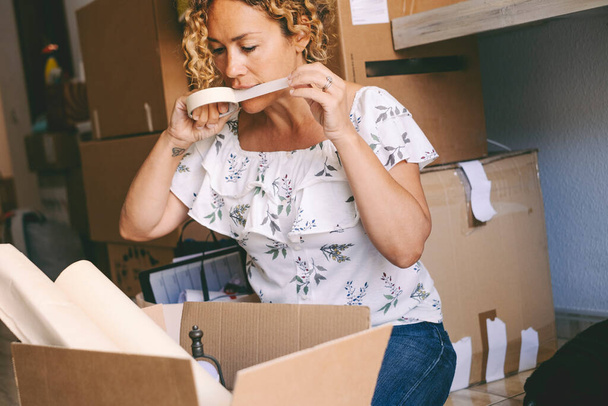  woman closing boxes at home for moving mortgage loan activity. Female people with carton boxes packing and unpacking stuffs for a move. New home and life concept. Young lady real estate owner - Fotó, kép