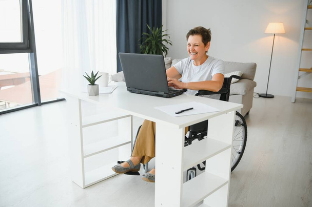 Freelancer in wheelchair using laptop near notebook and papers on table. - Foto, Bild