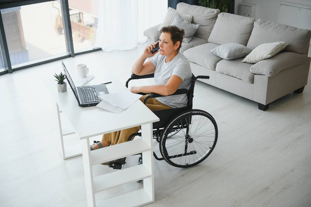 Middle age woman using laptop sitting on wheelchair at home. - Φωτογραφία, εικόνα