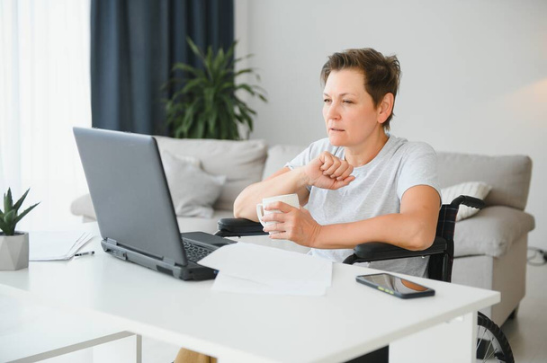 Middle age woman using laptop sitting on wheelchair at home. - Foto, immagini