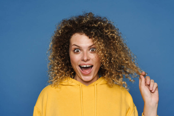 Young blonde woman dressed in hoodie expressing surprise at camera isolated over blue background - Foto, Imagem