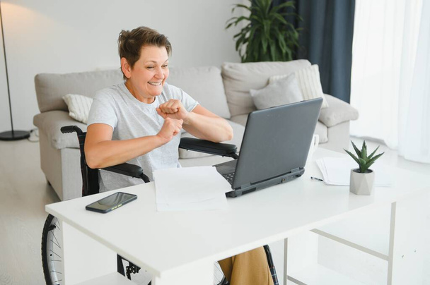 Middle age woman using laptop sitting on wheelchair at home. - Fotografie, Obrázek