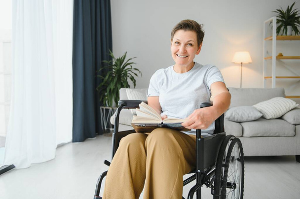 Tiro de uma mulher idosa sentada em uma cadeira de rodas e livro de leitura em casa. - Foto, Imagem