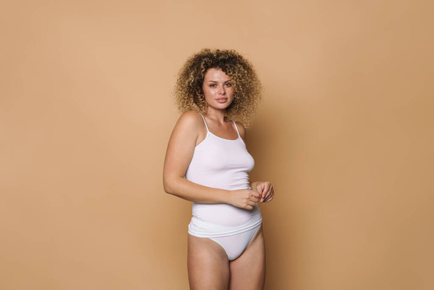 Young curly woman dressed in underwear looking at camera isolated over beige background - Fotografie, Obrázek