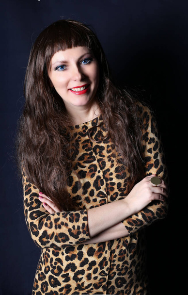 Long legged photomodel in leopard minidress and black stockings posing in studio - Foto, imagen