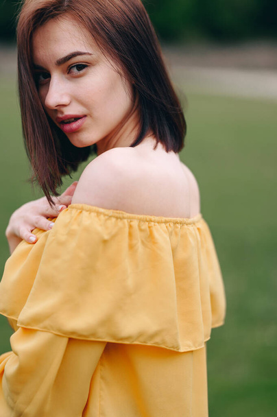 A Young Woman Stands Sideways in a Yellow Blouse. Hair covers half of the face. Soft blurred background. Advertising Cosmetics. Facial Skin Care - Zdjęcie, obraz