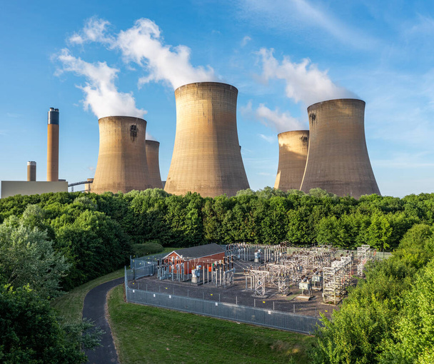 An aerial view of the cooling towers and chimney of a large coal fired power station generating electricity with electrical equipment to supply power to the national Grid via transformers - Photo, Image