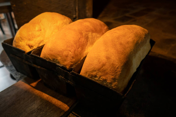 Close-up on a wooden shovel of freshly baked bread in metal molds in a traditional brick oven - Valokuva, kuva