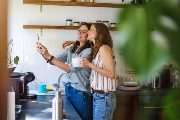 Két nő mobilt használ otthon a konyhában. - Fotó, kép