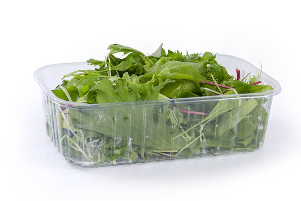 Mix of the different leaf vegetables in the transparent plastic container on a white background, side view - Foto, Bild