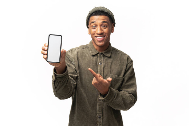 Positive confident man pointing at smartphone with white empty display, bragging with application. Indoor studio shot isolated on white background - Foto, Bild