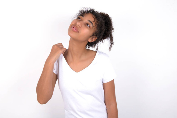 Young beautiful girl with afro hairstyle wearing white t-shirt over white background stressed, anxious, tired and frustrated, pulling shirt neck, looking frustrated with problem - 写真・画像