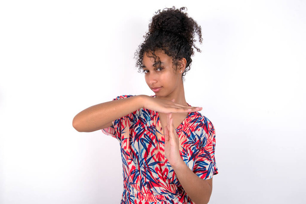 girl feels tired and bored, making a timeout gesture, needs to stop because of work stress, time concept. Young beautiful mixed race woman wearing colourful dress over white wall - Zdjęcie, obraz