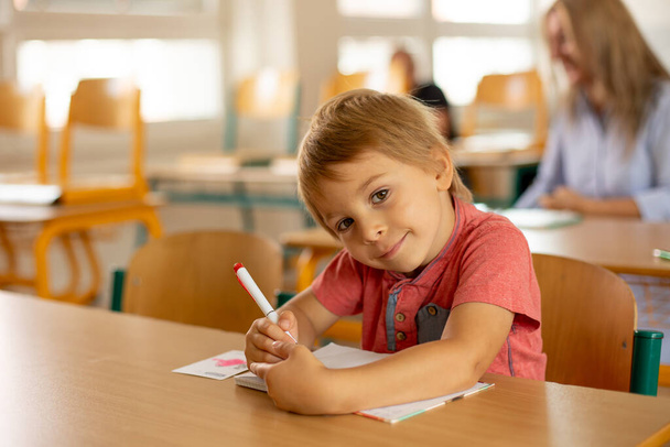 Preschool child, sitting on a desk at school, having lesson, learning new things - Φωτογραφία, εικόνα