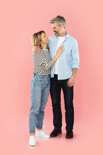 Glückliche Ehepartner mittleren Alters umarmen sich stehend vor rosa Hintergrund im Studio. Mann und Frau posieren für ein Familienangebot in der Werbung. Ehe und romantische Beziehung - Foto, Bild