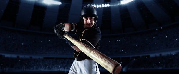 Powerful hit. Front camera view of of professional baseball player with baseball bat in action during match in crowed sport stadium at evening time. Sport, win, winner, competition concepts. - Photo, Image