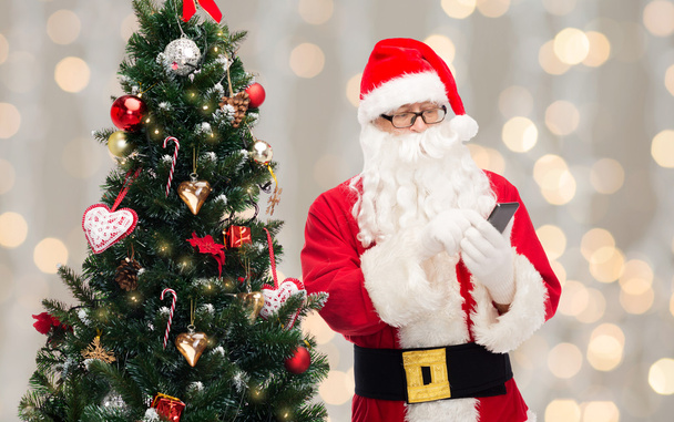 santa claus with smartphone and christmas tree - Φωτογραφία, εικόνα