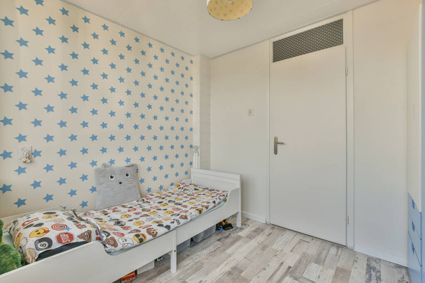 Interiér bílého pokoje s dětskou postýlkou a modrým wardopem v blízkosti okna za denního světla - Fotografie, Obrázek