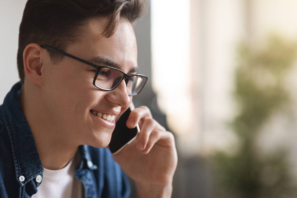 Κοντινό πλάνο του χαμογελώντας Millennial Guy σε γυαλιά ηλίου μιλώντας στο κινητό τηλέφωνο, νεαρός όμορφος άντρας κάνοντας τηλεφώνημα, θετικός άνθρωπος έχοντας ευχάριστη συνομιλία, απολαμβάνοντας την κινητή επικοινωνία, αντίγραφο χώρου - Φωτογραφία, εικόνα