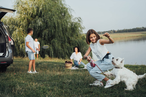 Menina adolescente brincando com West Highland White Terrier Dog no fundo de sua família se divertindo ao ar livre na viagem de carro Minivan - Foto, Imagem