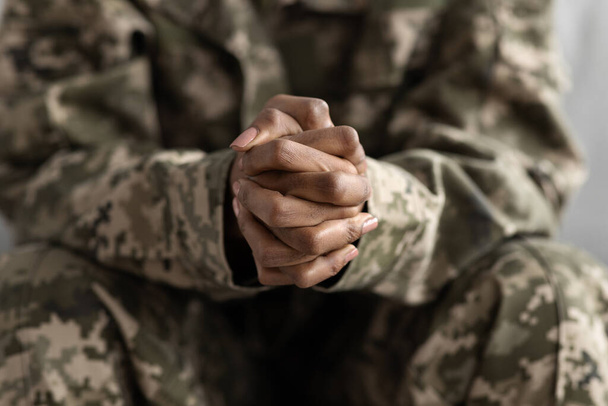 Close-up Shot van gebalde handen van onherkenbare zwarte vrouwelijke soldaat in camouflage leger uniform, Afro-Amerikaanse militaire vrouw zit op de bank, Selectife Focus op vuisten, Gehakte afbeelding - Foto, afbeelding