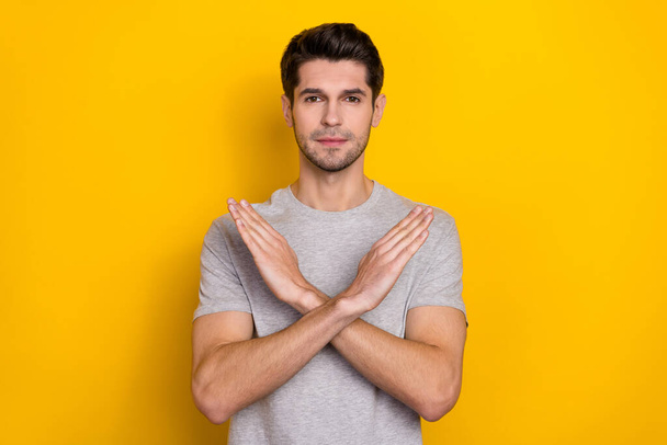 Photo of strict brunet millennial guy show no wear grey t-shirt isolated on yellow color background. - Foto, Imagen