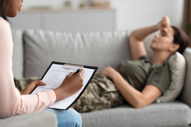 Black Psychiatrist Lady Having Psychotherapy Session With Depressed Military Woman Suffering Mental Health Problems, Filling Questionnaire, Upset Female Soldier In Uniform Lying On Couch - Photo, Image