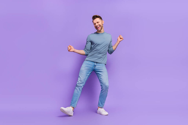 Photo of adorable lucky guy wear grey shirt having fun dancing rising fists isolated violet color background. - Zdjęcie, obraz