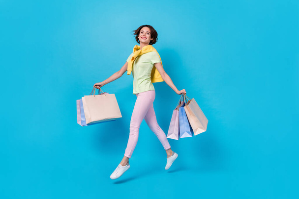 Full length photo of pretty young brunette lady run do shopping wear t-shirt pants footwear isolated on blue background. - Photo, image