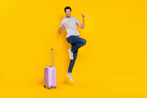 Full size photo of cool brunet millennial guy jump with bag wear t-shirt jeans shoes isolated on yellow background. - Photo, Image