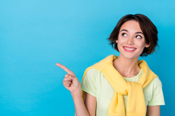 Photo of dreamy sweet lady dressed yellow pullover pointing finger looking empty space isolated blue color background. - 写真・画像