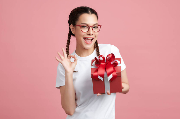 Feliz bonita mujer joven sosteniendo caja de regalo sobre fondo rosa, espacio de copia en blanco para su contenido publicitario. - Foto, imagen