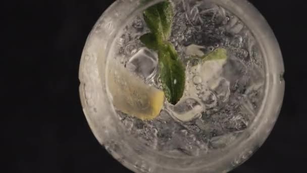 Blubbernde Zitroneneis-Minze-Cocktail-Spinning-Glas Nahaufnahme. Eiswürfel mit prickelndem Sodawasser in Superzeitlupe. Makroaufnahme von oben schwarzer Hintergrund. Erfrischendes Kaltgetränk im Sommer - Filmmaterial, Video