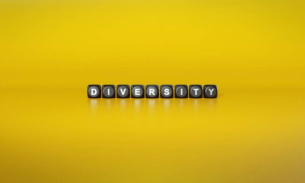 Слово Разнообразие прописано белым текстом на темных деревянных блоках на обычном желтом фоне - Фото, изображение