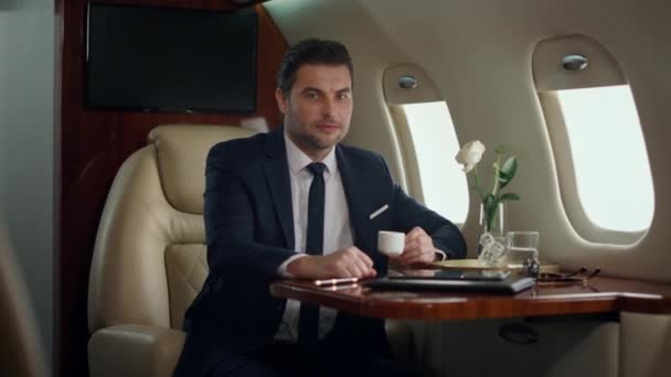 Mosolygó vezérigazgató egyedül pózol a repülőgép ablakánál. A sikeres ember élvezi a céges utazást. Magabiztos, elegáns üzletember, első osztályú luxus öltönyben. Elegáns úriember pihen az úton - Felvétel, videó